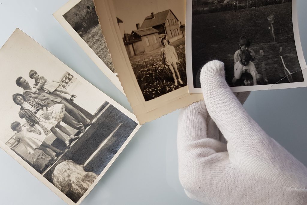 hand with white gloves on holding three photographs and one photo on the table below
