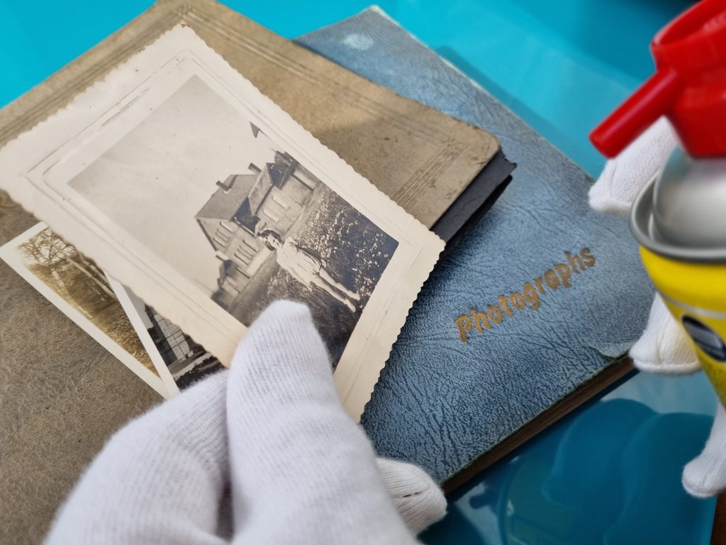 air pressure cleaner being pointed at an old photograph. Photo albums behind it