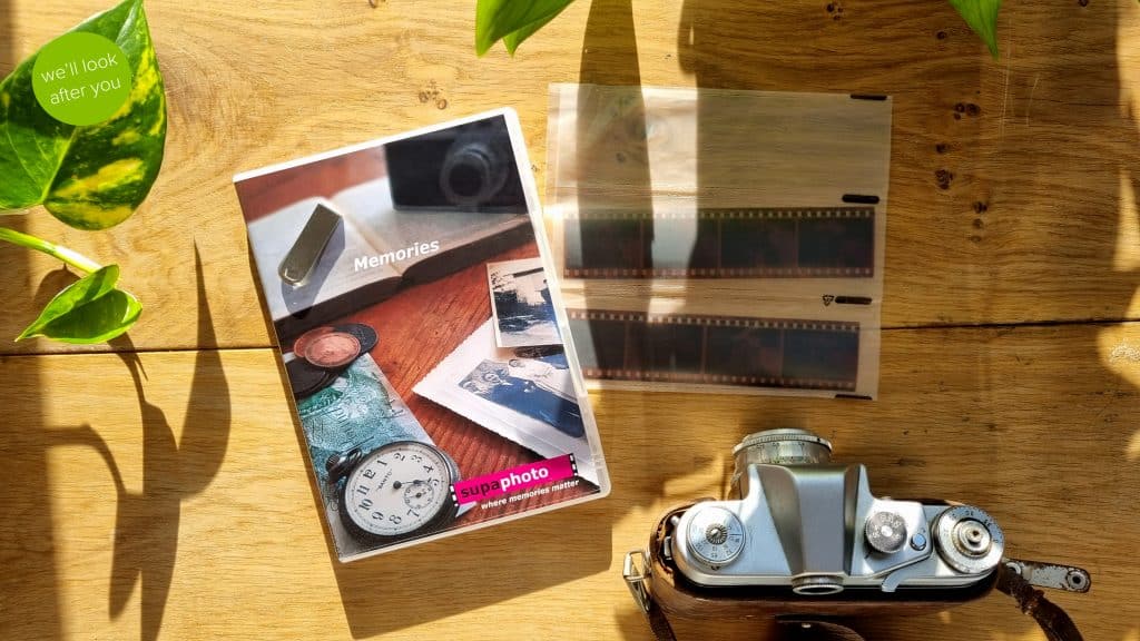 a vintage camera, two negatives and a dvd case with a memory stick on a wood background