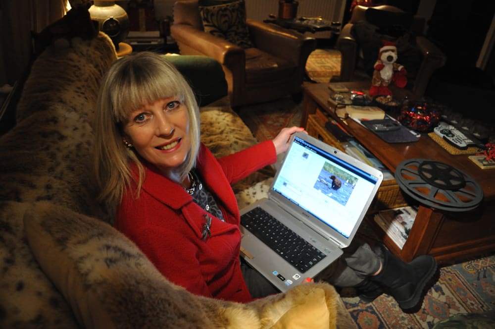 woman sitting in a dark room with a laptop showing a video and cine reel on the table