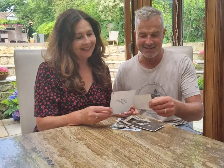 Man and woman smiling at photographs with a pile of photos on the table beside them