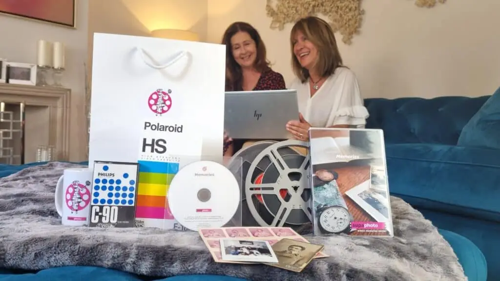 a collection of cine film reels, a supaphoto bag, dvd and CD all on a sofa with two smiling women in the background.