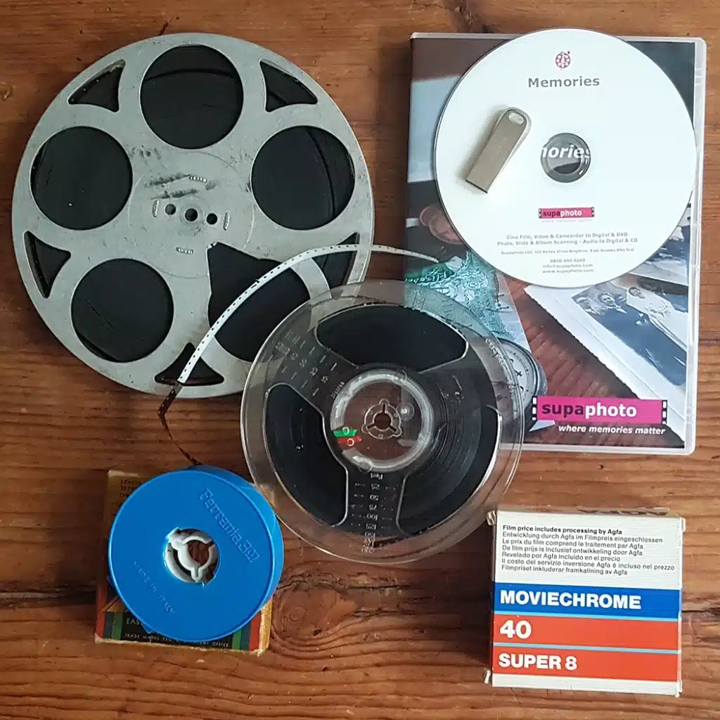 A close up of various cine film spool reels with film including 8mm, super 8, 9.5mm and 16mm on table with DVD Case & USB - cine film transfers