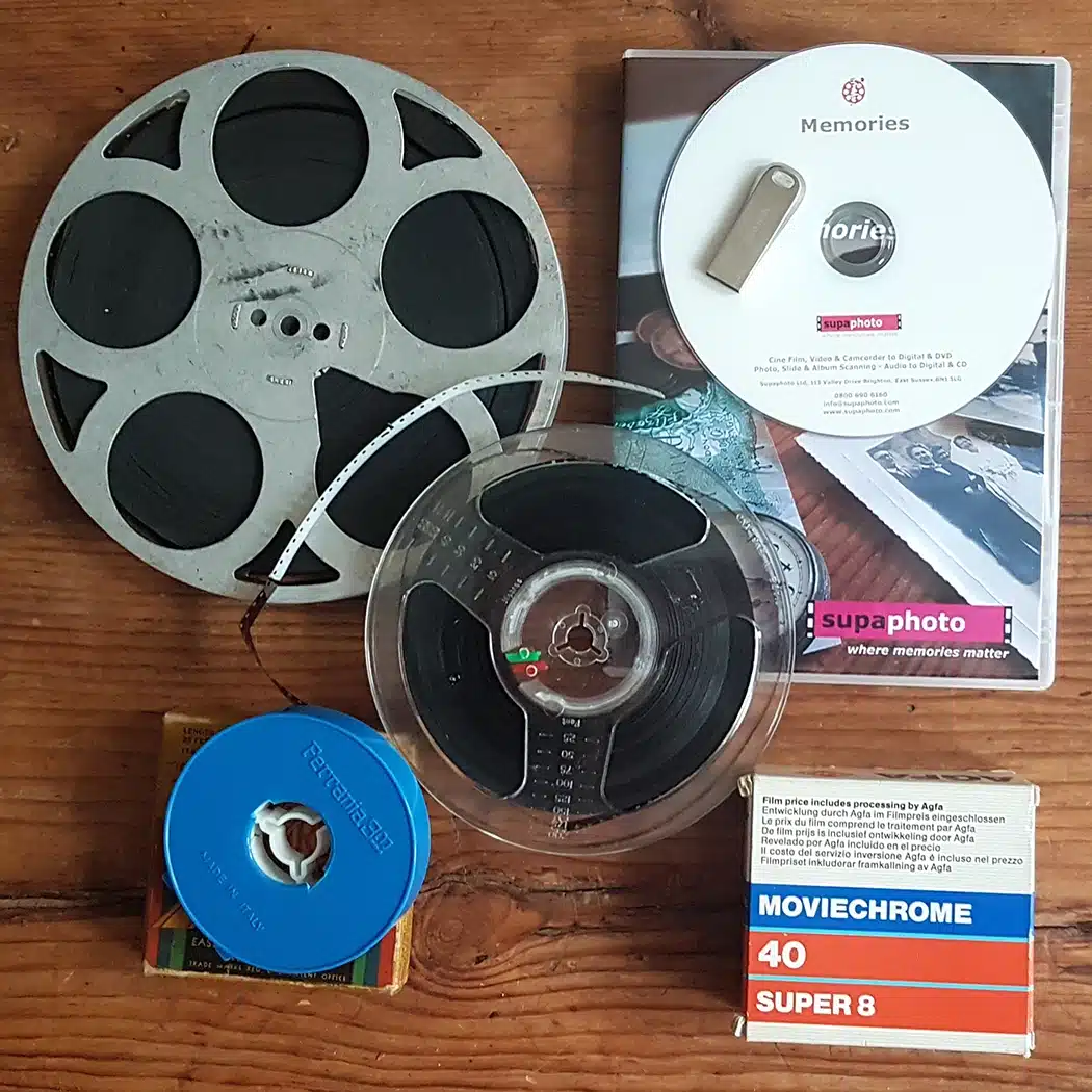A close up of various cine film spool reels with film including 8mm, super 8, 9.5mm and 16mm on table with DVD Case & USB - cine film transfers
