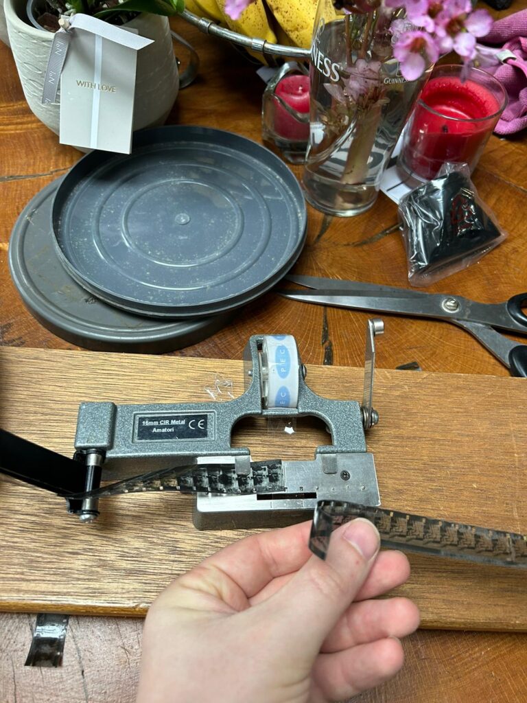 Image of cine film splicing being done on a wooden table with flowers in the background.