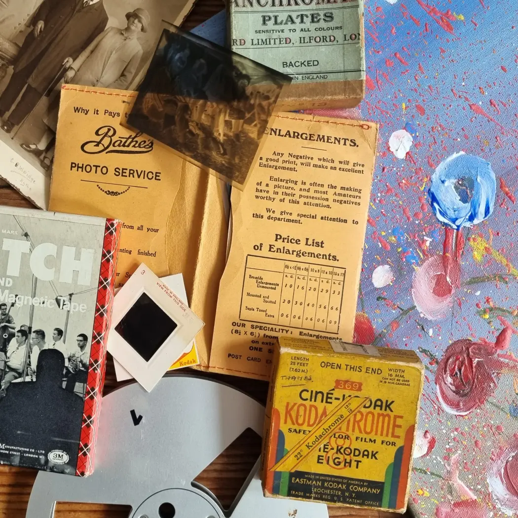 A collection of vintage photographic materials and media, including negatives, slides, film reels, and archival paperwork arranged on a table.