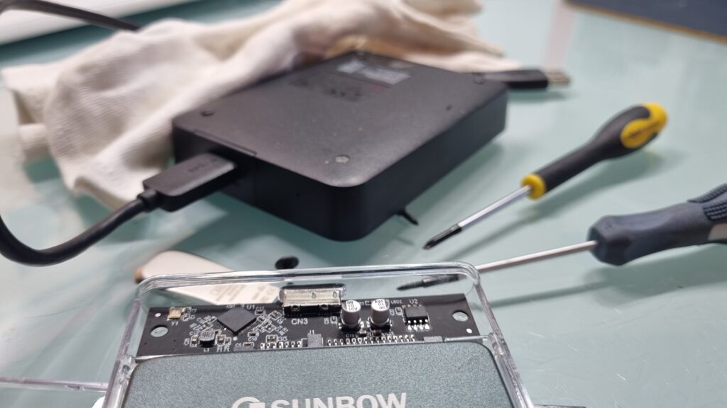 External storage device and disassembled SSD enclosure on a desk with screwdrivers, used for data conversion and duplication.